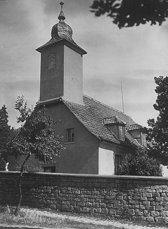 Schwarz-Weiß-Abbildung einer Dorfkirche, vor der Kirche eine Natursteinmauer.