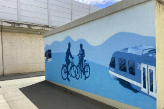 Blaues Wandbild auf dem zwei Fahrradfahrer, eine Regionalbahn und ein Linienbus gesprüht wurde