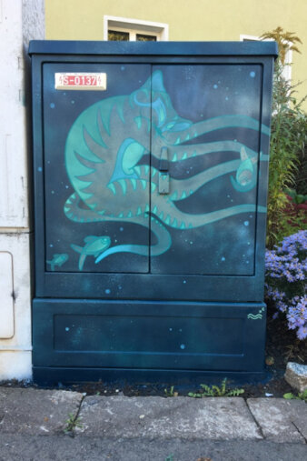 Graffiti-Projekt Medienkasten gestaltet mit ein blauen Qualle, die eine Fisch fängt.
