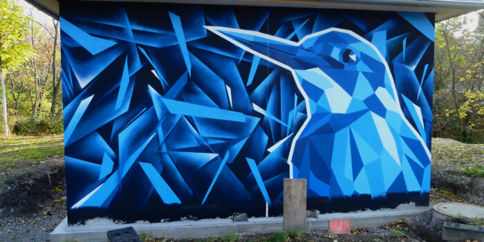 Graffiti-Projekt mit Spraydosen wurde ein Eisvogel in Blautönen an die Fassade einer WC-Anlage gesprüht