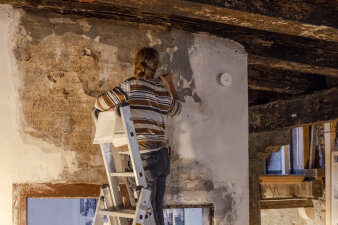eine Person steht auf einer Leiter und bearbeitet eine Inschrift an einer Wand