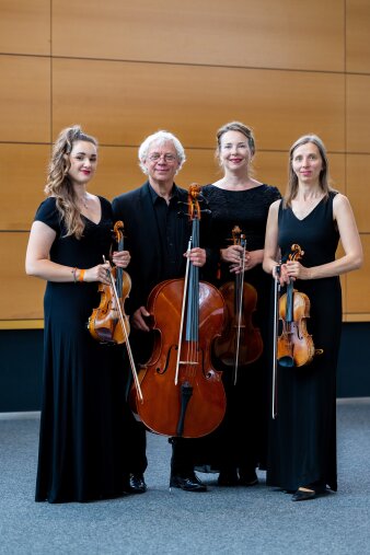 4 Musiker mit ihren Instrumenten stehen vor einere Holzwand