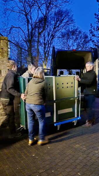 mehrere Personen verladen eine Tiertransportkiste auf ein Fahrzeug