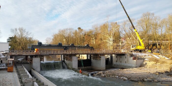 ein Kran steht an einem Fluß und errichtet eine Brücke sowie ein Wehr