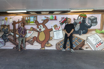 zwei Männer stehen vor einer mit Graffiti gestalteten Wand in einem Tunnel