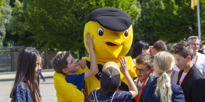mehrere Kinder umringen eine lebensgroße Werbefigur, einen gelben Vogel