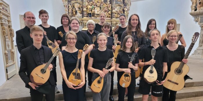 Ein Ensemble aus Jugendlichen und Erwachsenen hält mehrere Zupfinstrumente in der Hand. 