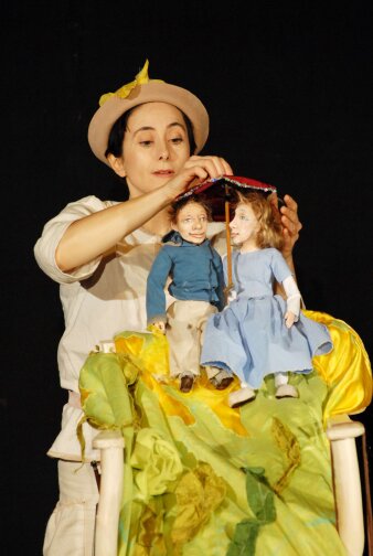 eine Puppenspielerin mit zwei Holzsspielpuppen, die Mann und Frau unter einem Schirm darstellen