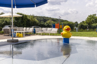 flaches Baby-Schwimmbecken mit großer gelber Ente und Sitzmöglichkeiten im Hintergrund