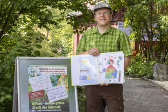 ein Mann hält einen aufgeschlagenen Ordner mit bunten Zeichnungen