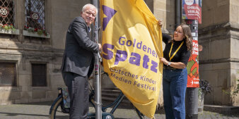 Ein Mann und eine Frau hissen eine gelbe Flagge vor dem Erfurter Rathaus