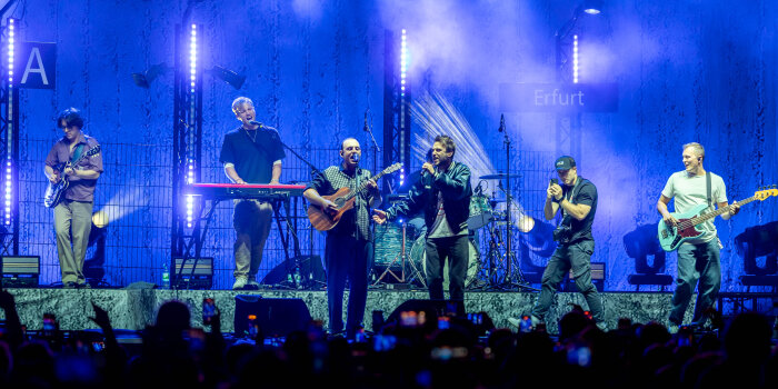 Sechs Musiker stehen auf einer beleuchteten Bühne