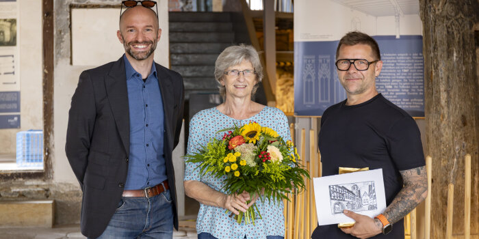 zwei Männer und eine Frau, die einen bunten Blumenstrauß in der Hand hält