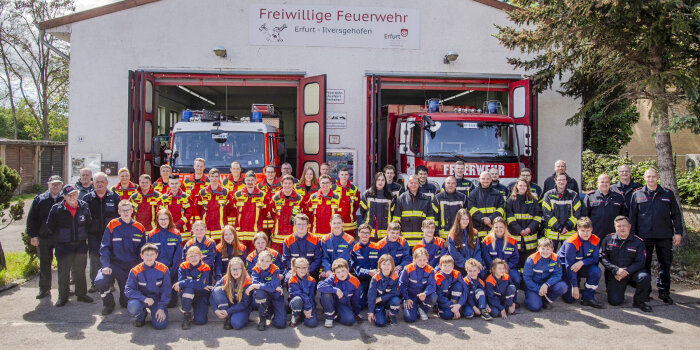 Vor einem Feuerwehrgerätehaus sind viele Erwachsene und Kinder in Feuerwehruniform zu sehen. 
