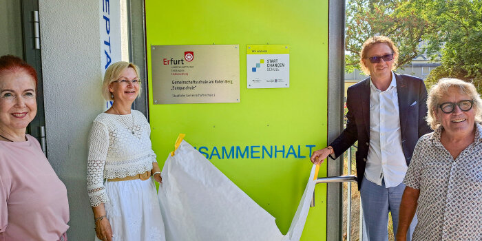 Zwei Männer und zwei Frauen enthüllen ein Schild an einer Wand. 