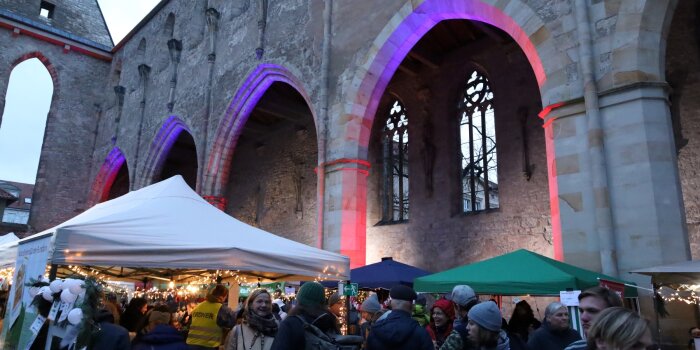 viele Menschen stehen vor einem alten Gemäuer, im Hintergrund Verkaufsstände