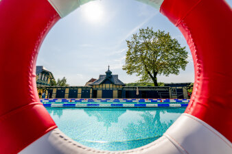 Blick durch einen Schwimmreifenauf auf ein mordernes Schwimmbecken, umgeben von historischen Bauten