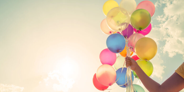 Hand mit bunten Ballons vor Himmel