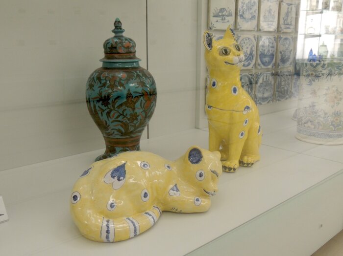 Glasvitrine mit zwei gelben Figuren in Katzenform un dahinter einer Vase